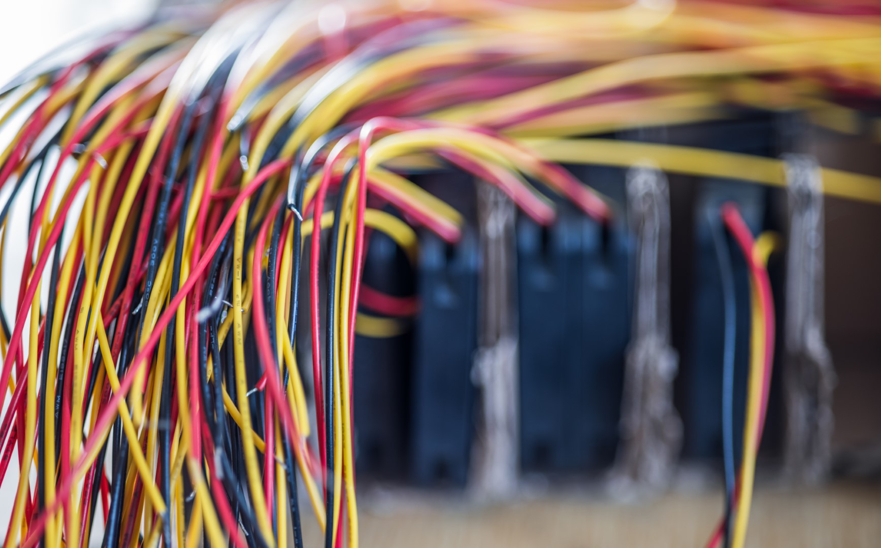 A close-up view of a bundle of thinly wires with color connections sticking out of a blurred electronic panel.