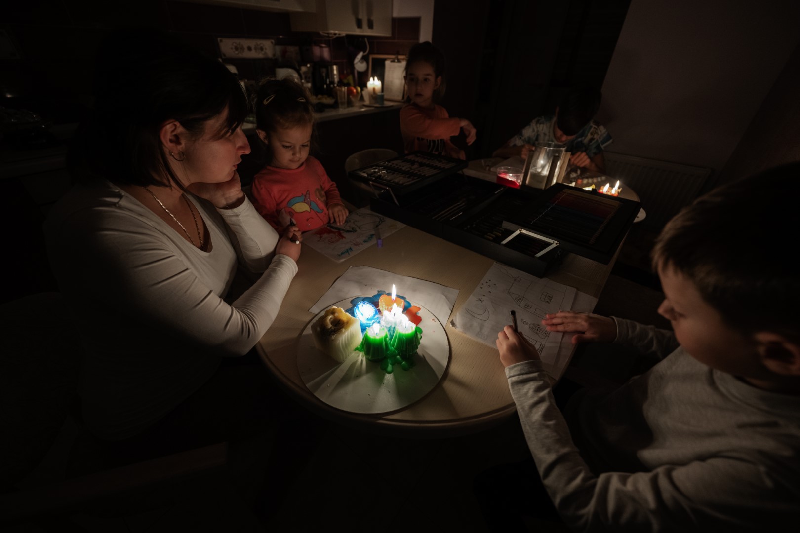 A family spending time together during a blackout with many candles on the table while the kids are drawing.