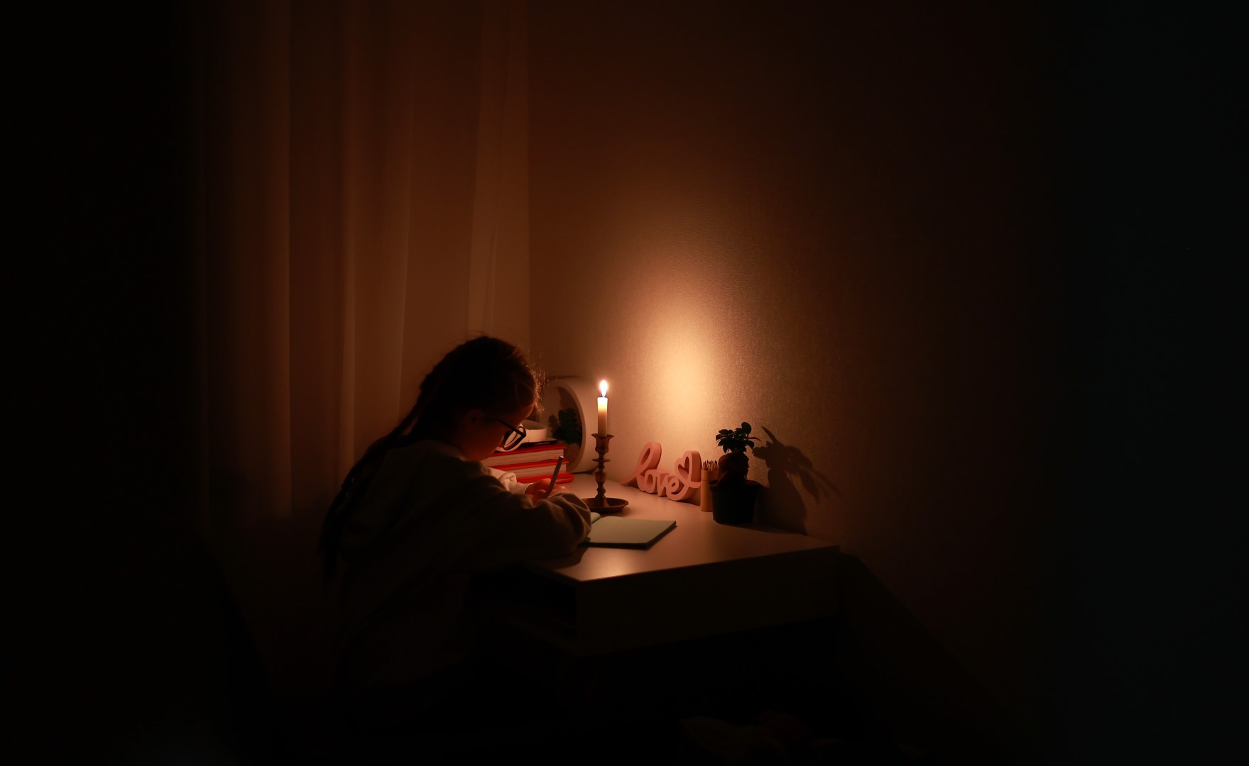 A girl uses candlelight to do homework in darkness during a blackout.