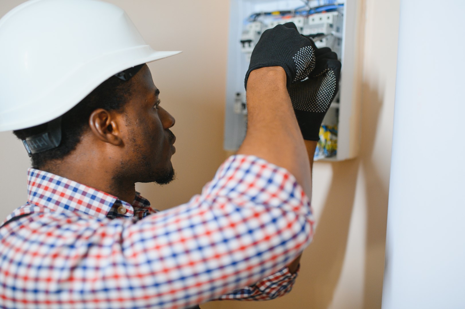 A male electrician works in a switchboard with an electrical connecting cable.