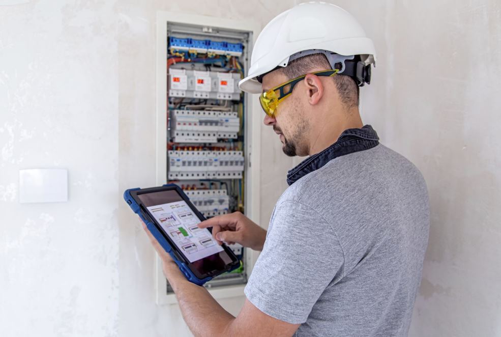 An electrical technician looks focused while connecting the tablet to a switchboard to program the new smart installations.