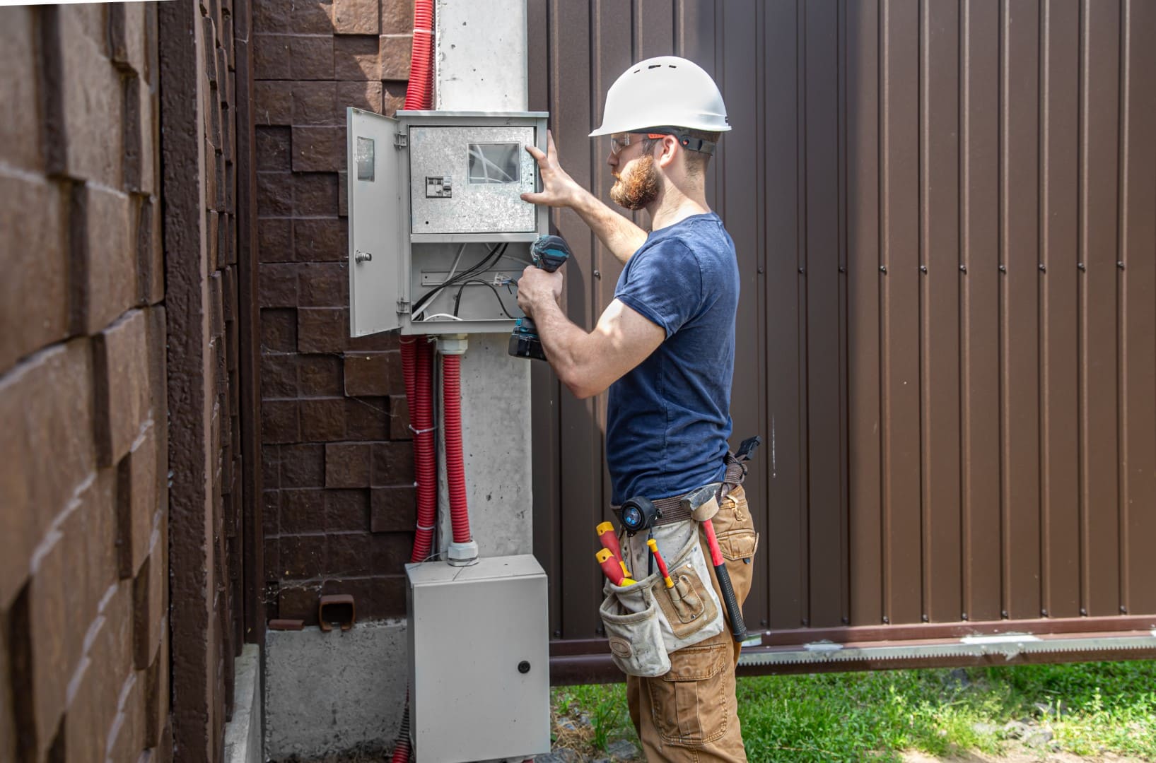 An electrician wearing a protective helmet examines the cables of an electrical box.