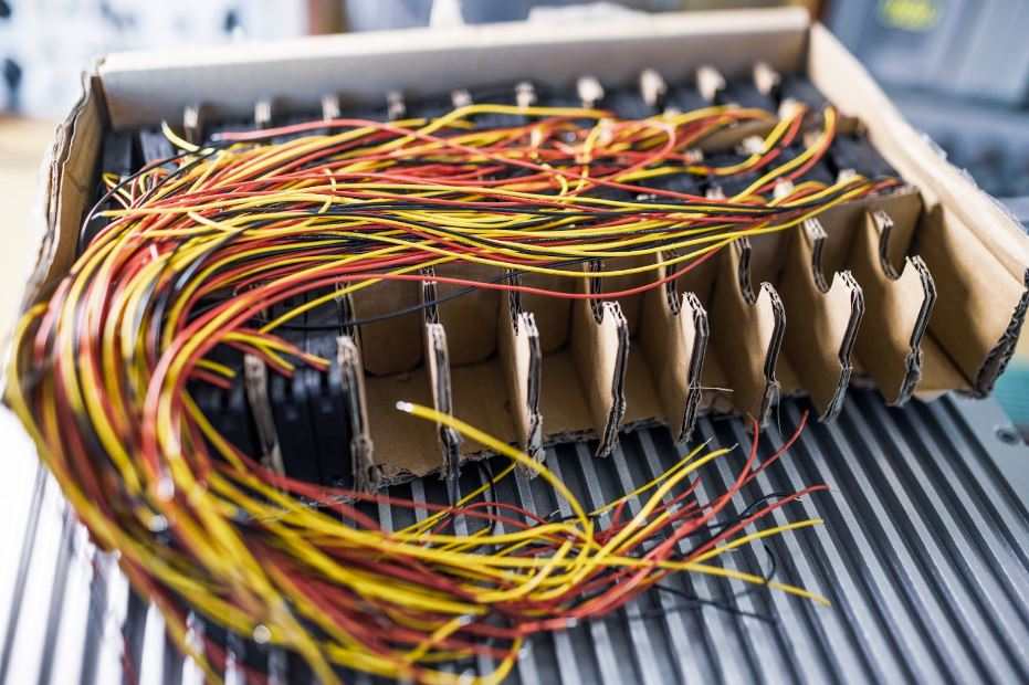 A bundle of thin, cut electric wires with various colored connections arranged in a box, set against a blurry background.