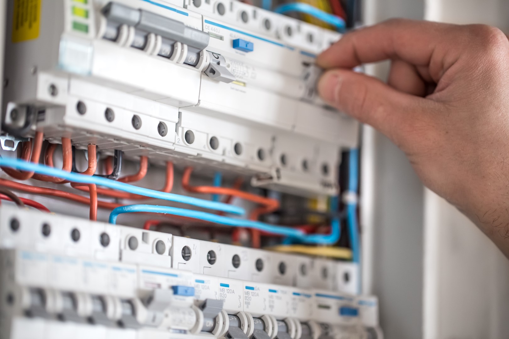 A cropped view of a man’s hand working on a switchboard with fuses.