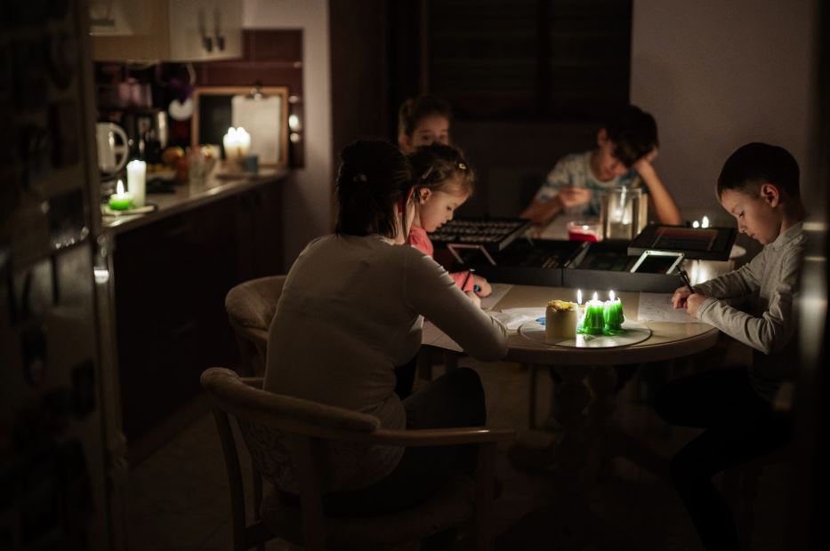 A family of five gathers around a round table during a power outage. The boys study by candlelight while the parents and young sister look on.