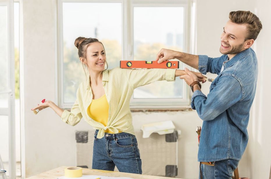 A happy young couple having fun using a leveler during home repairs, sharing smiles and laughter as they work together.