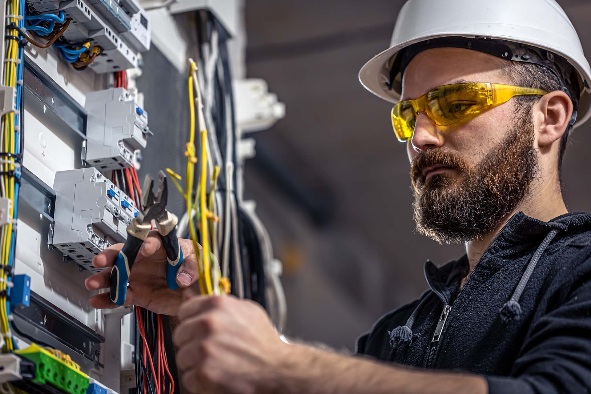 A male electrician fixes the switchboard with a pair of electrical pliers and an electrical connecting cable.