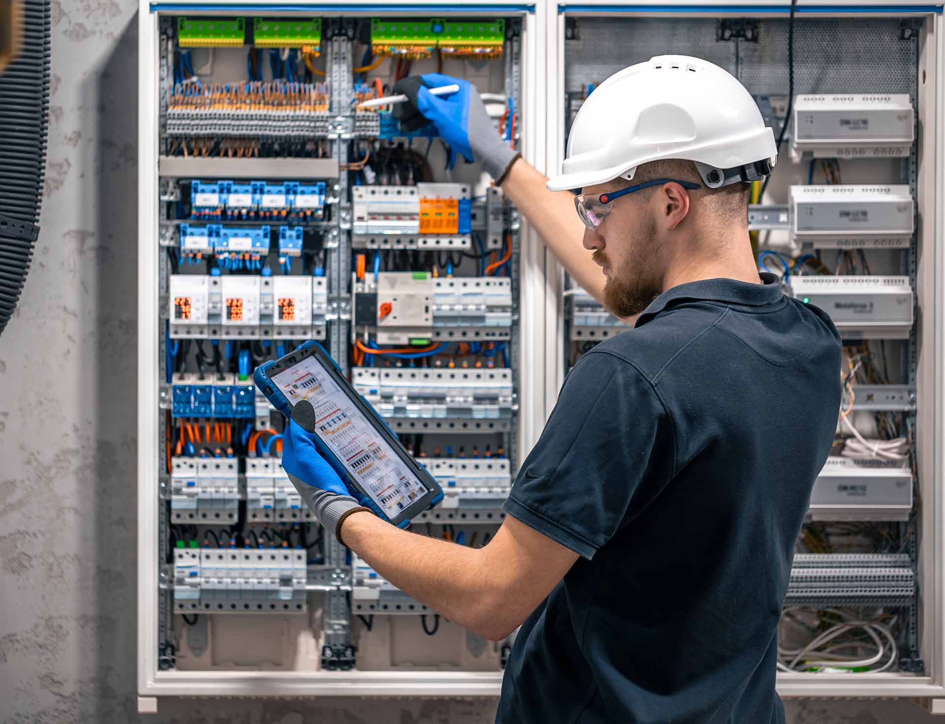 A male electrician is checking a switchboard by turning on switches.