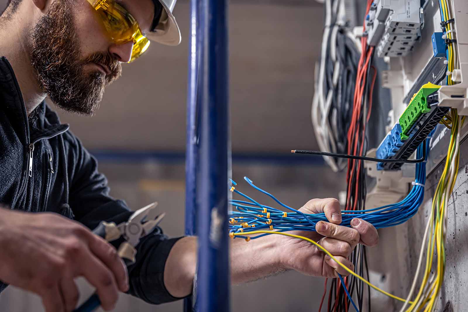 A male electrician is working on a switchboard with an electrical connection to the cable.