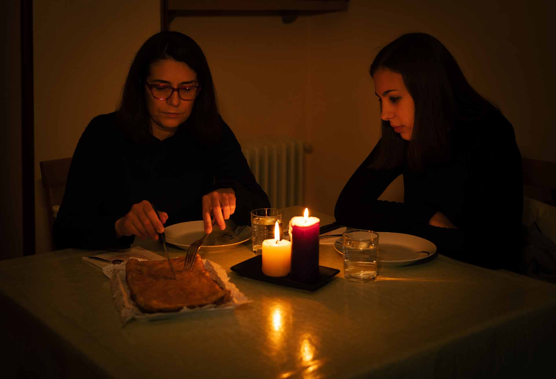 A mom and daughter are eating dinner with candlelight during a blackout.