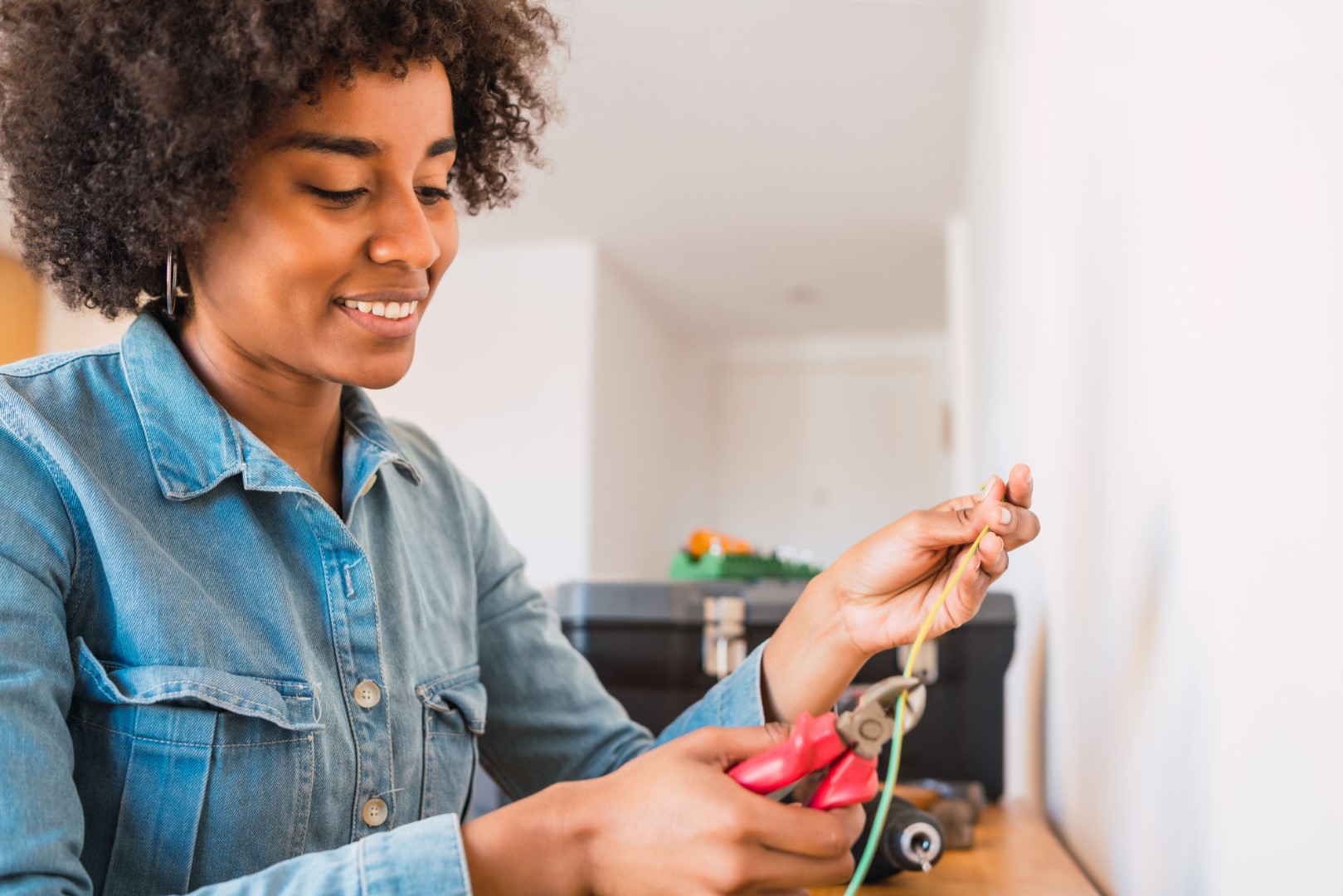 A woman in a jean jacket uses wire cutters to cut an electrical cable.