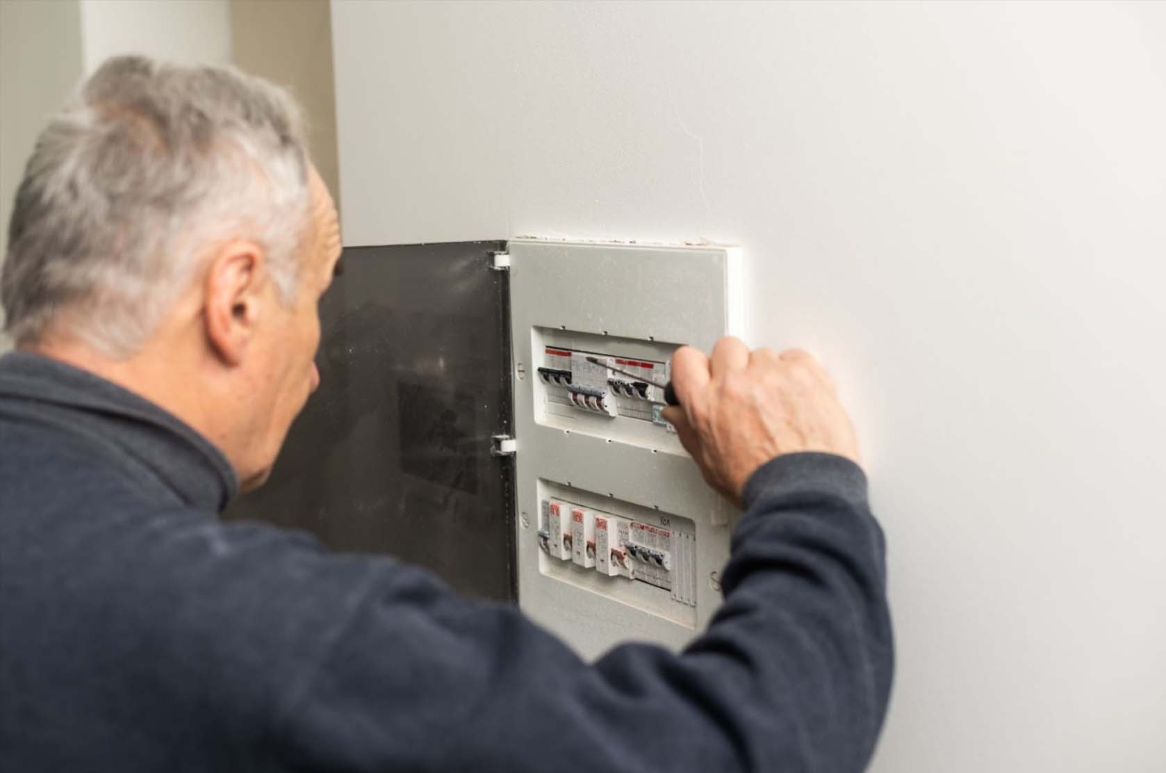 An elderly man in a black long-sleeve shirt fixing an electric meter, showcasing an example of household electrical repairs.