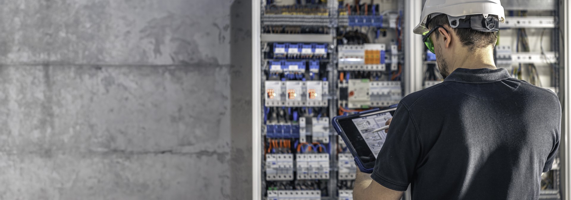 An electrician working on installing and programming a switchboard using a smart tablet.