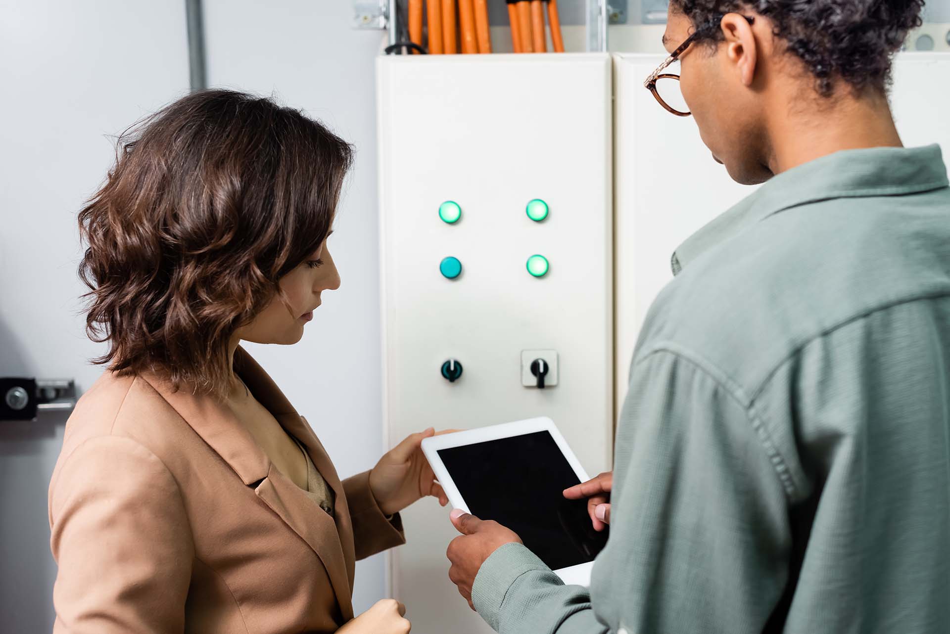 An engineer shows a report to her manager while checking the switchboard.