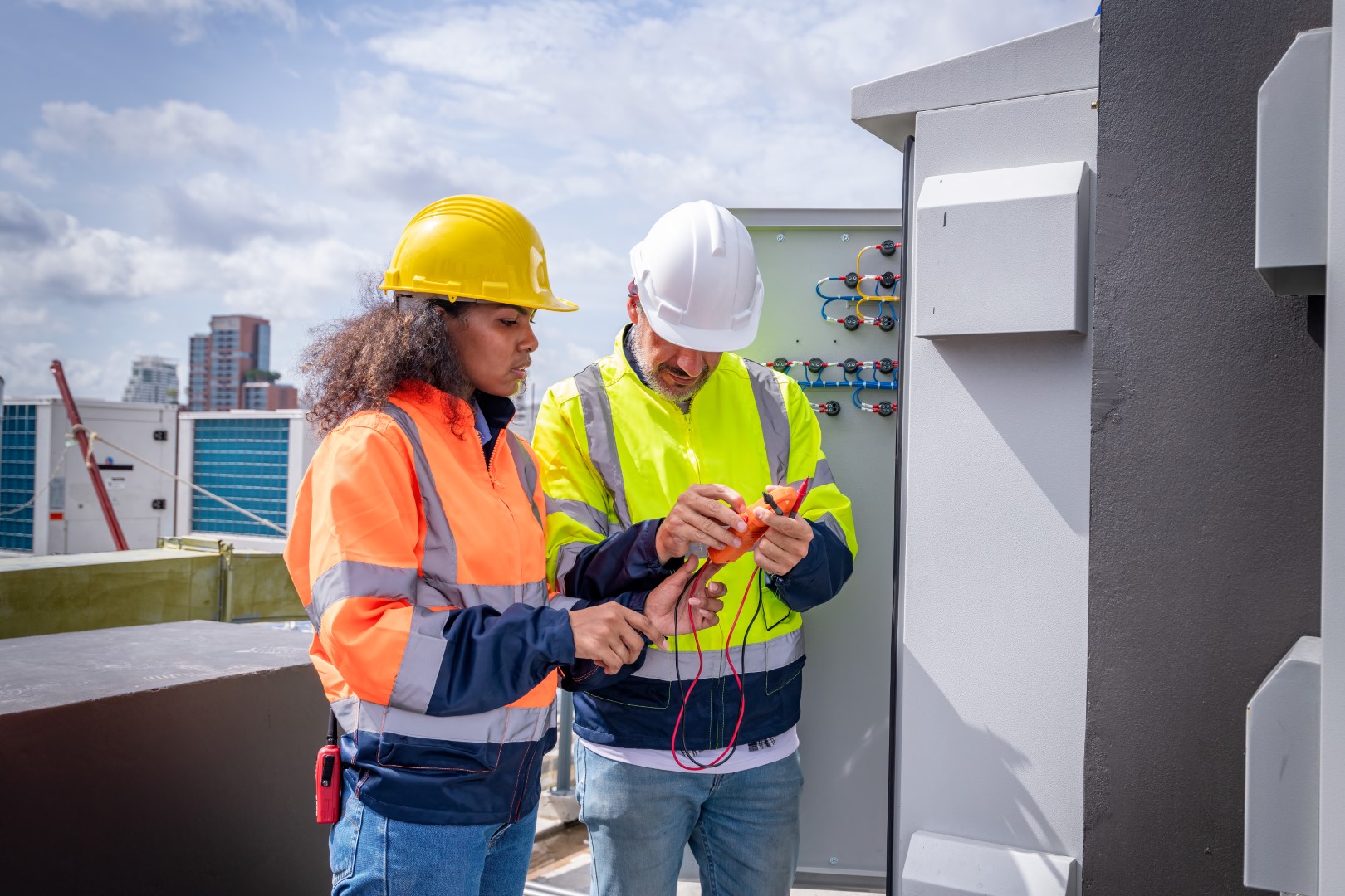 Two electricians in hard hats and uniforms checking and inspecting electrical equipment.