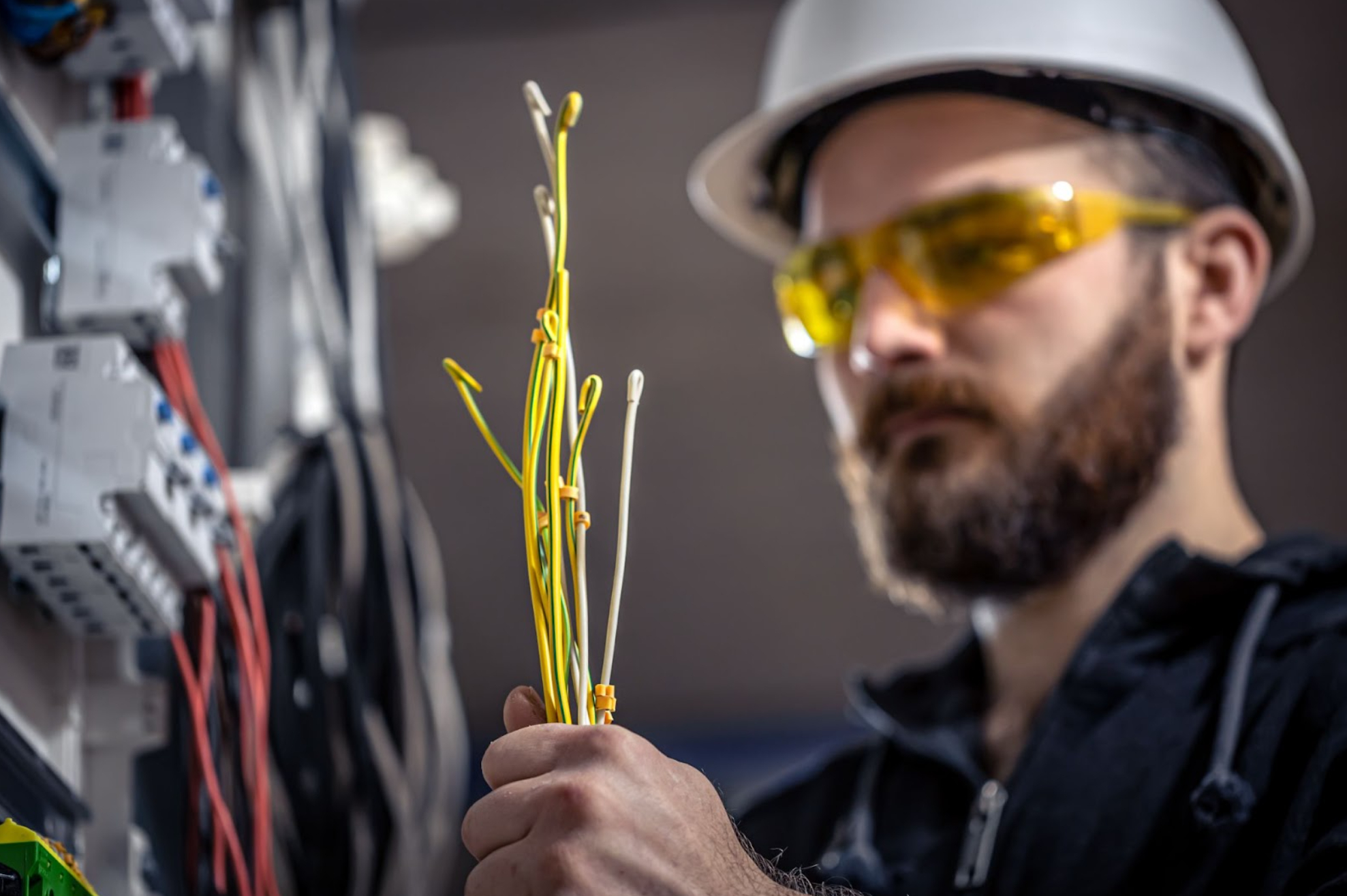 Man with a hardhat and goggles holding wiring.