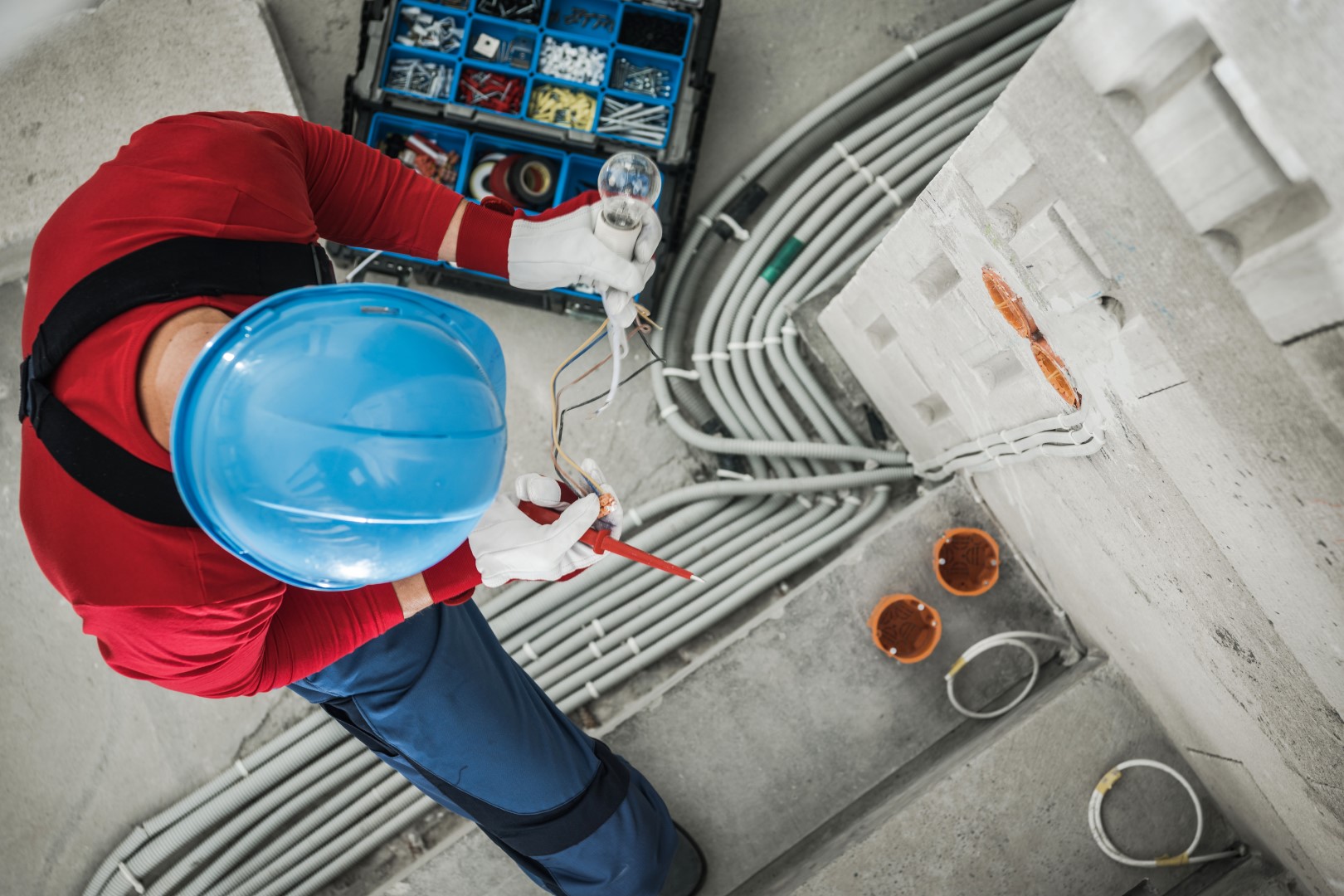 Aerial view of an electrician wearing a blue hardhat and overalls checking wires during an electrical installation.