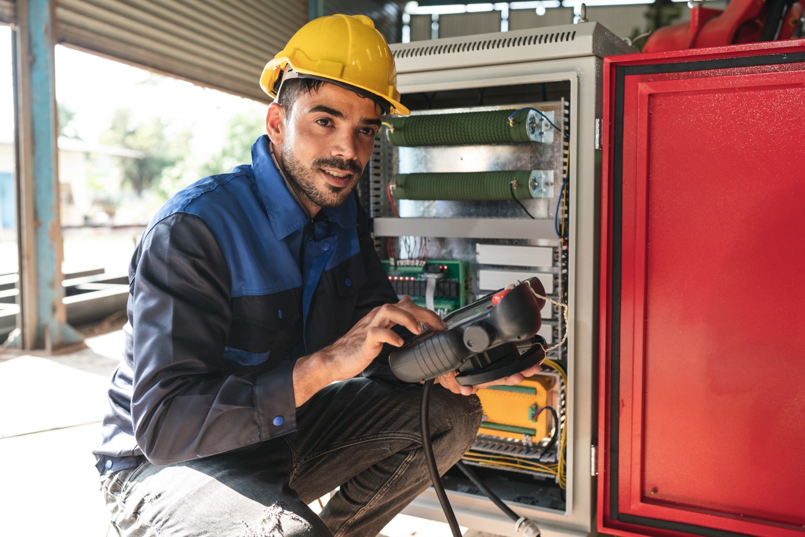 An engineer wearing a yellow hat checks and runs a factory diagnostic test using an electronic machine.