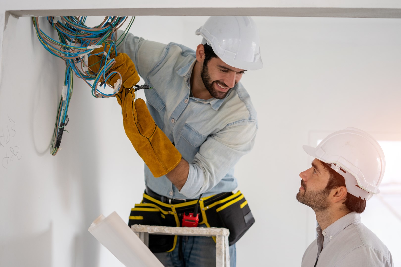 Two electrical engineers wearing white hardhats working to install wiring.