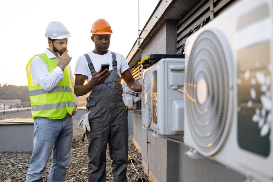 Two technicians on a roof next to an HVAC system.