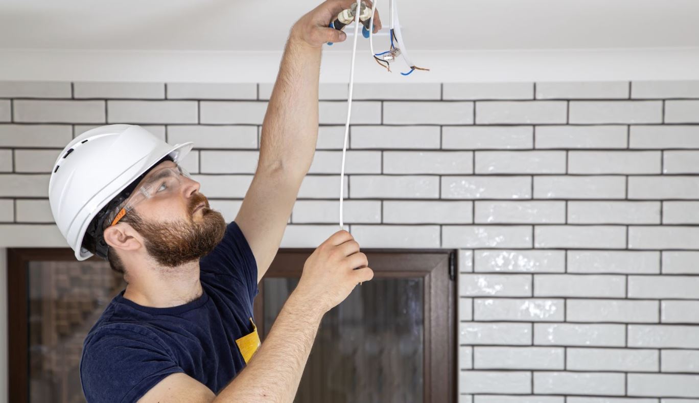 Man in a hard hat working with wiring in a home.