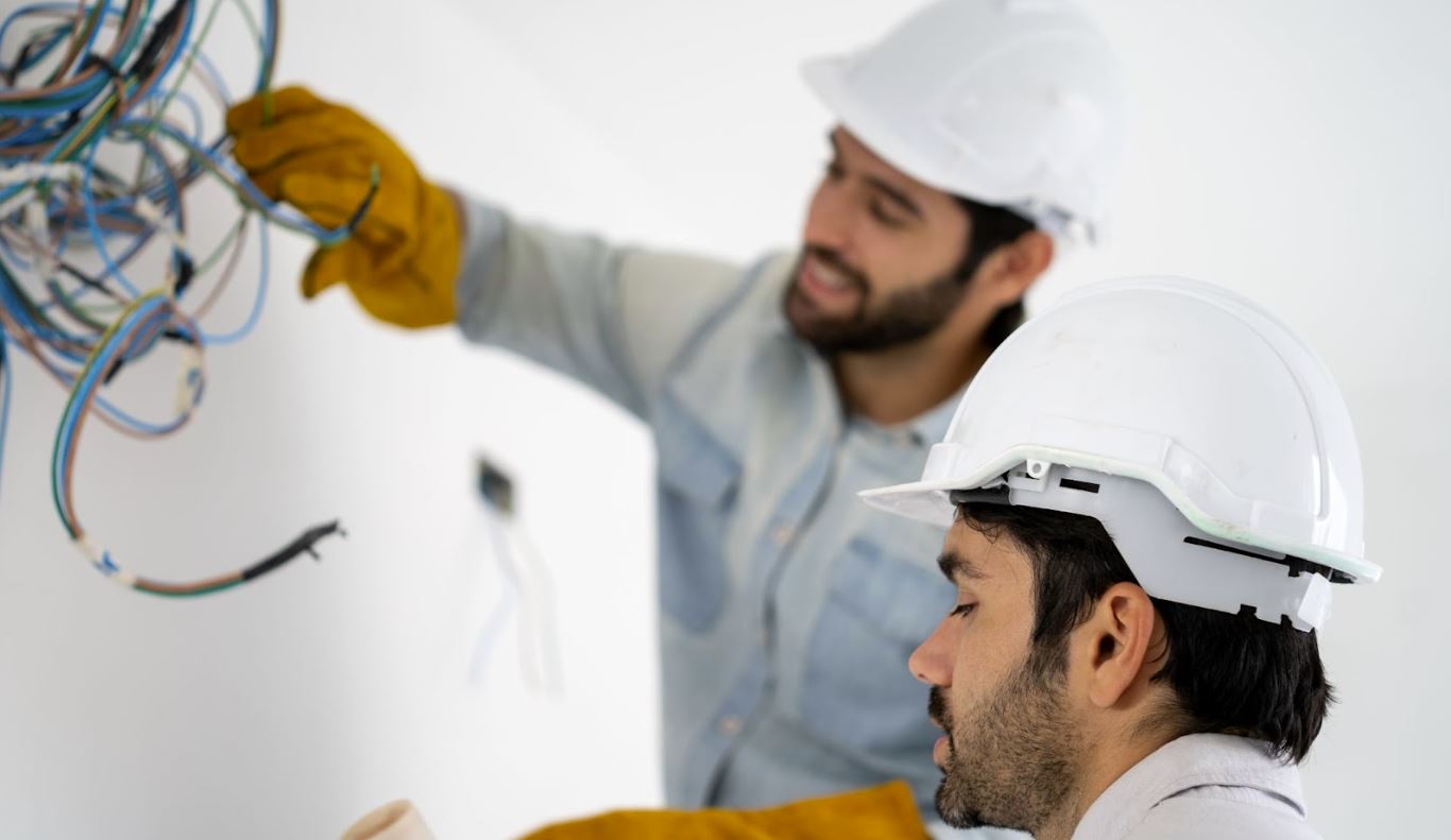 Two men in hard hats working with wiring.