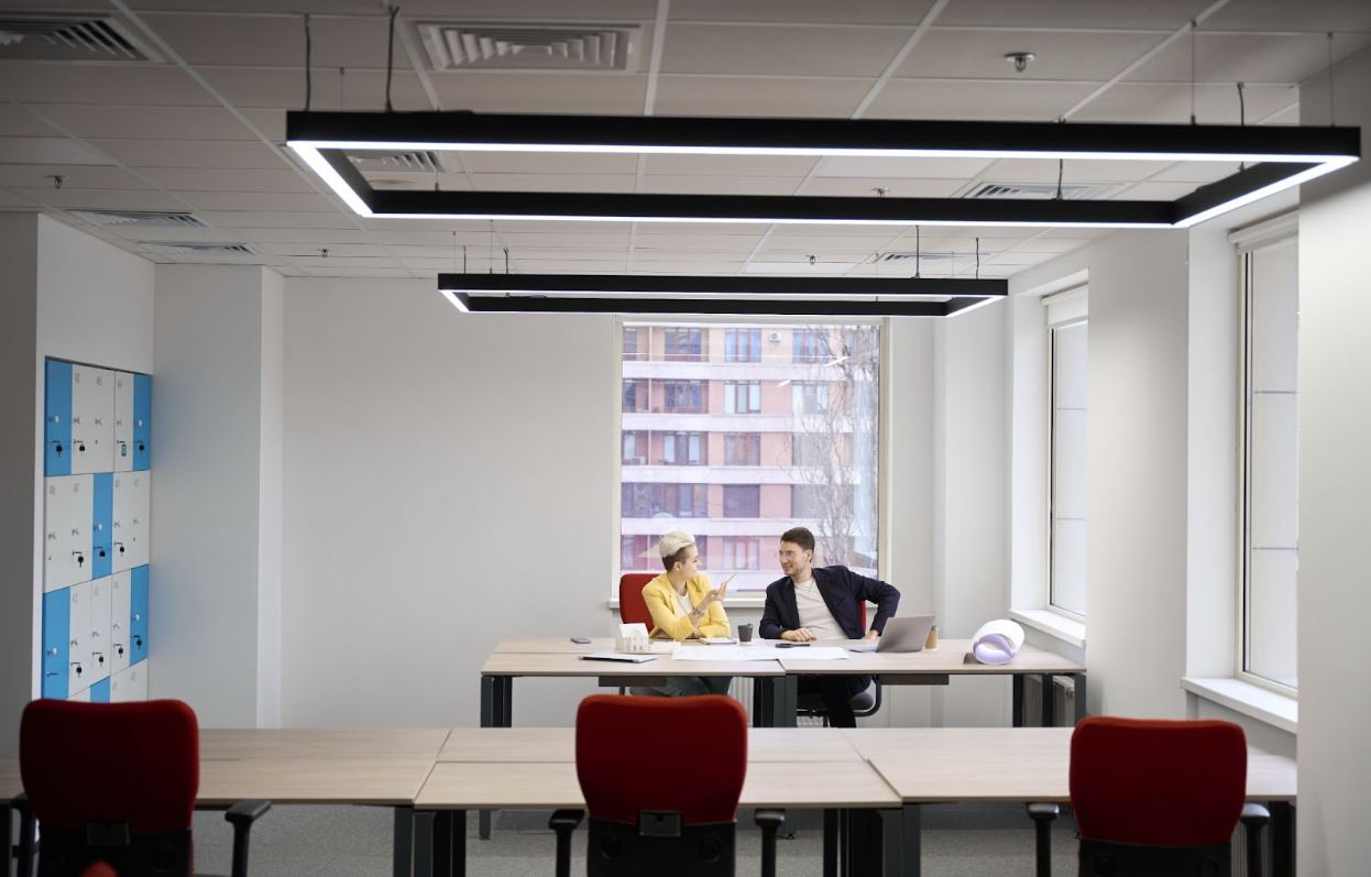 Two people sitting in an office space with LED lighting above.