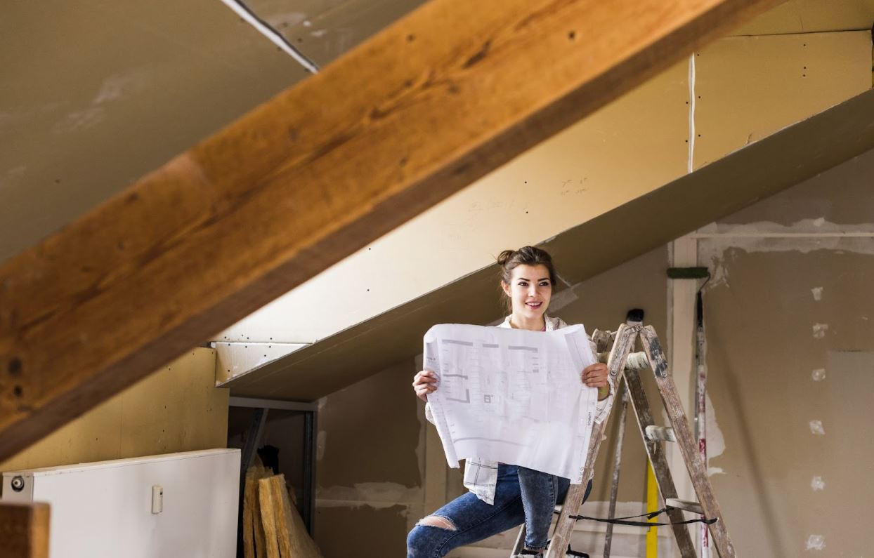 Woman holding up a piece of paper while sitting on a ladder in her home undergoing renovations.